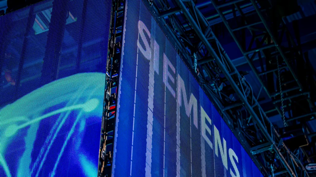 Angled corner view of a Sparks-designed Siemens LED video wall at CES 2025 — illuminated Siemens wordmark meeting a second panel with geometric arrow motifs in electric blue and cyan.
