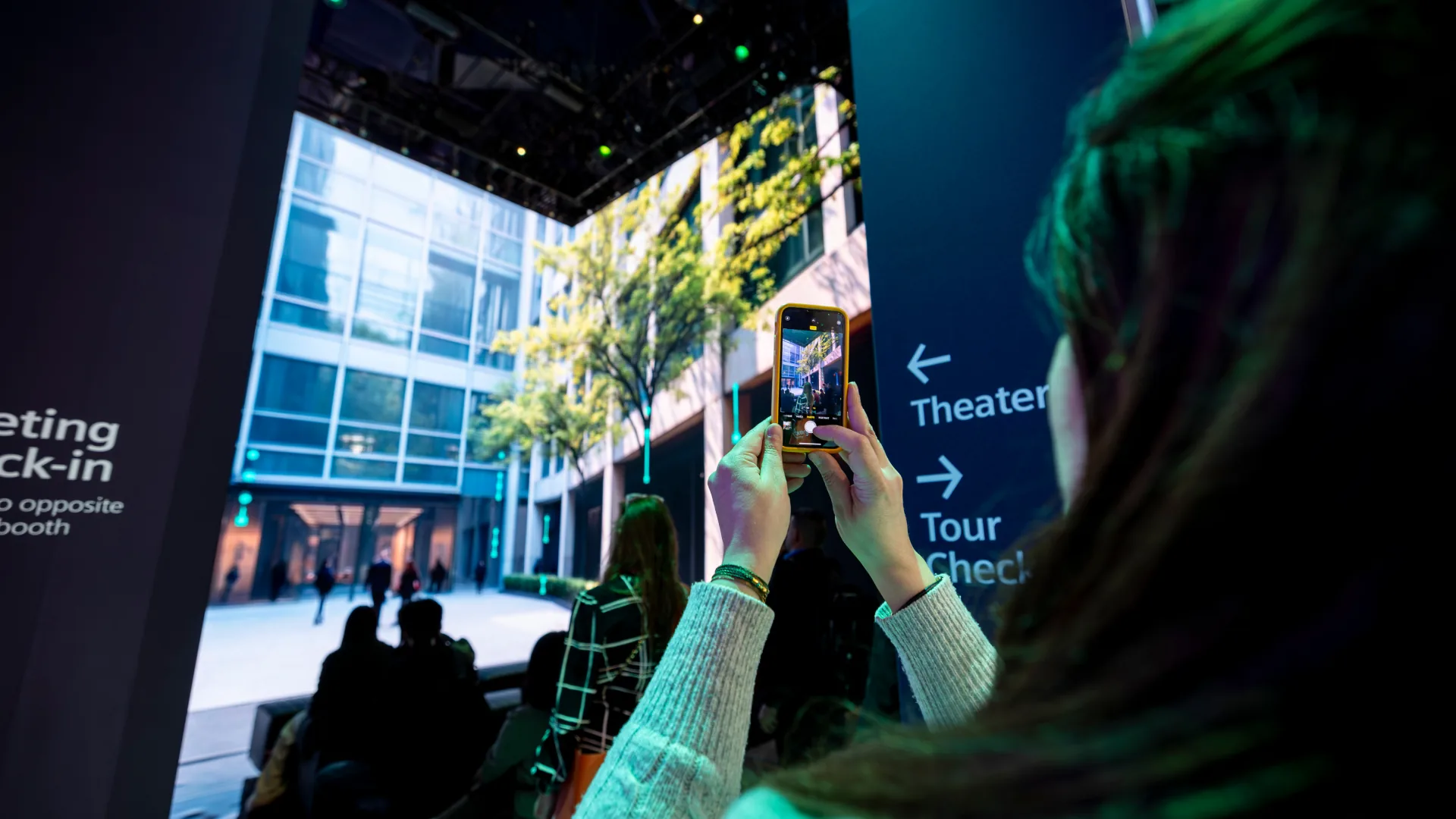 Guest films a screen showing a tree-lined building near the Theater sign