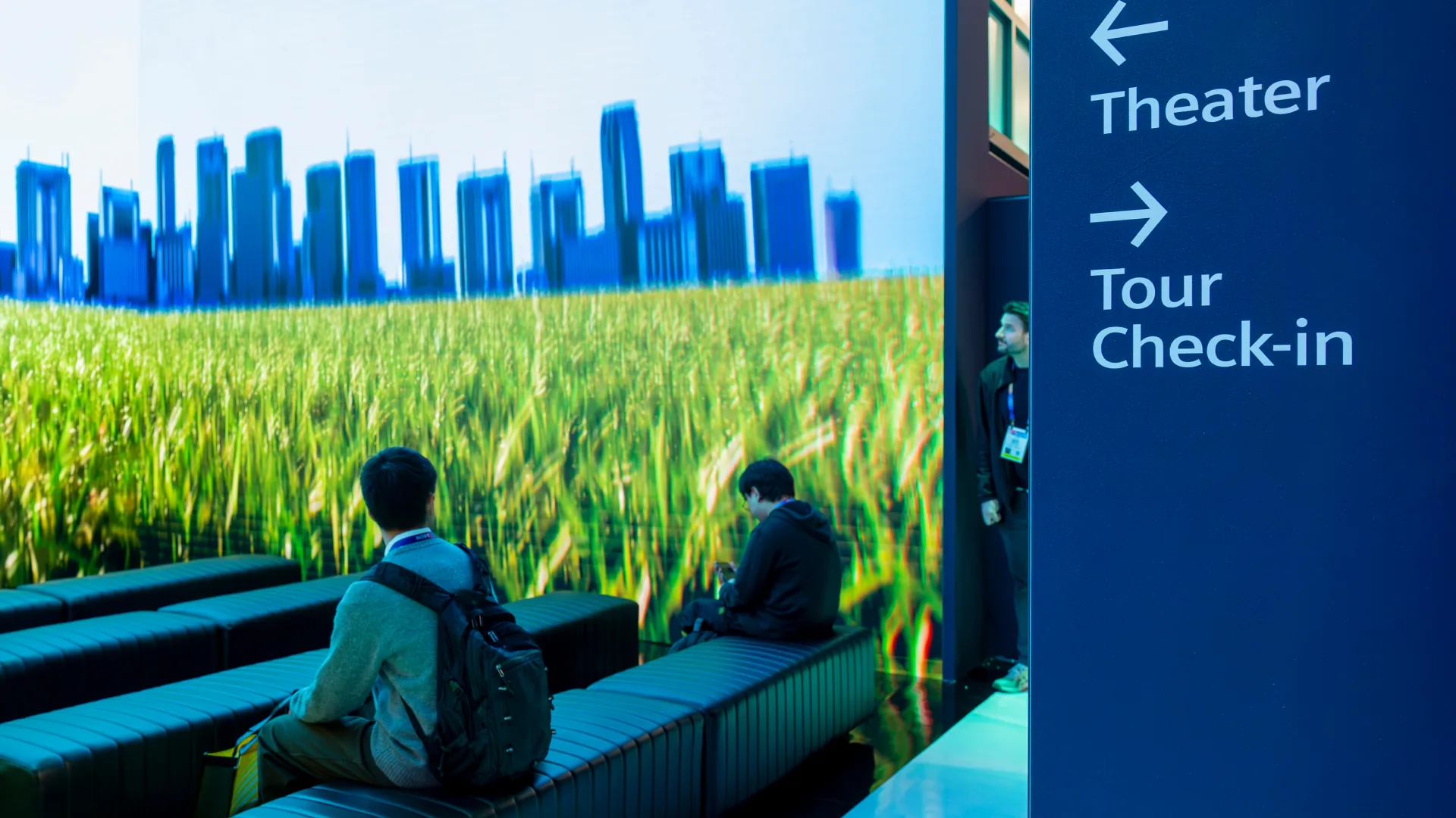 Two visitors rest on theater benches facing a wheat field and skyline