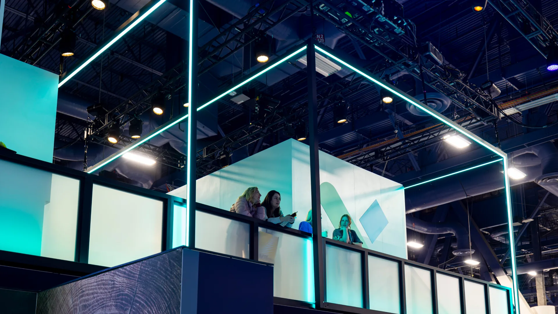 Upper-level glass meeting rooms framed in neon light above the exhibit floor
