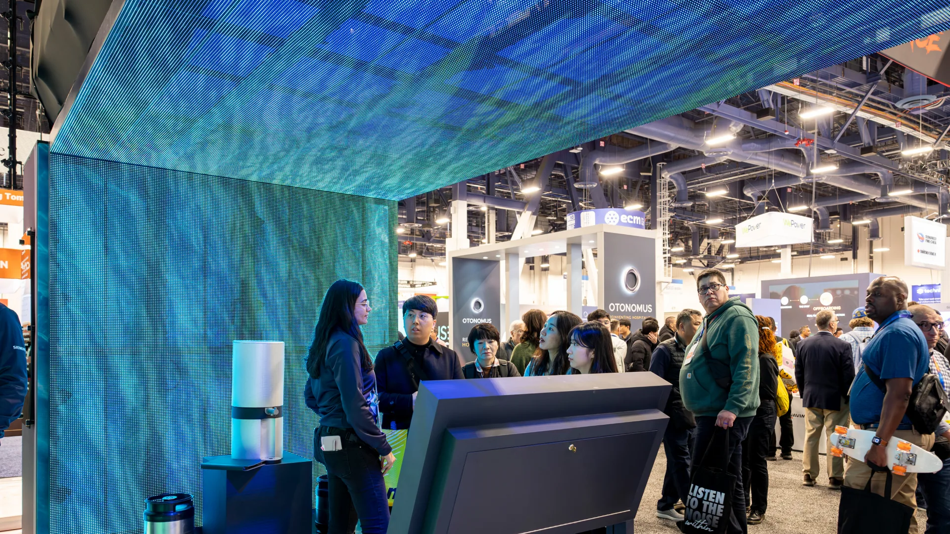 Guide talks with visitors at a counter under a water-pattern LED canopy