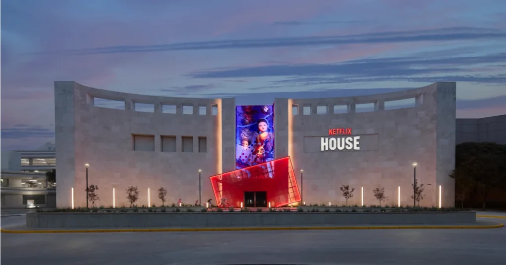 Symmetrical wide view of the Netflix House Dallas facade at dusk with the central vertical mural and the red angular entrance portal.