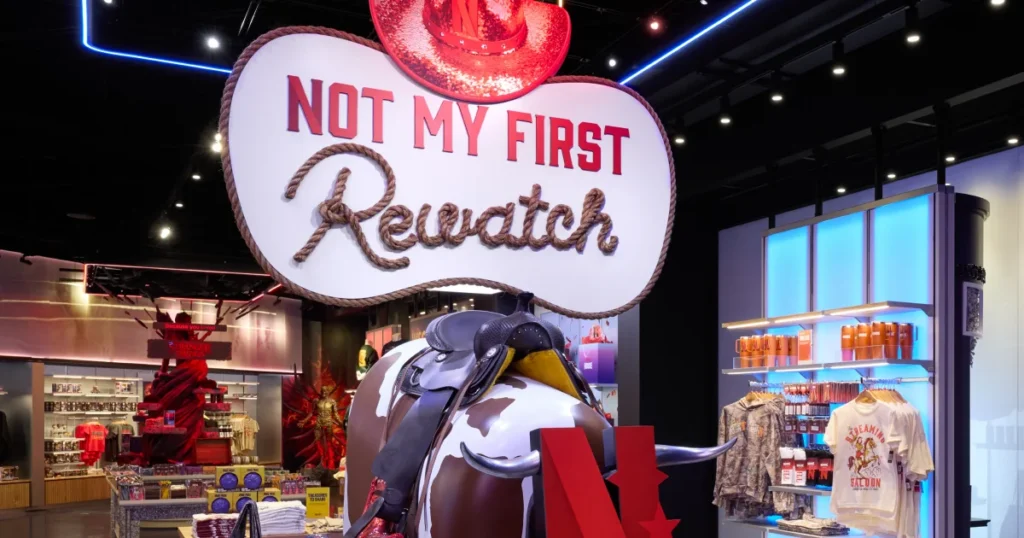"Not My First Rewatch" retail centerpiece at Netflix House Dallas featuring a saddled cowhide bull figure, sparkly red cowboy hat signage, and Western-themed Screaming Saloon merchandise.