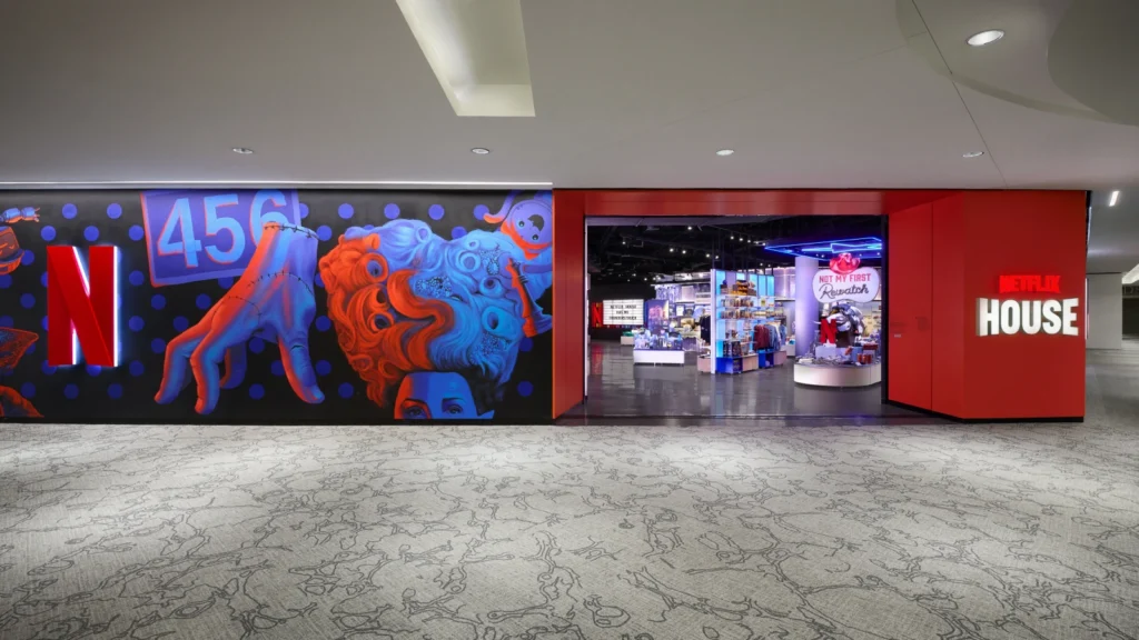 Squid Game mural corridor leading to the Netflix House Dallas retail entrance — featuring the "456" iconography and Wednesday graphics, "Not My First Rewatch" signage, and Netflix House wordmark. Sparks-designed retail experience.