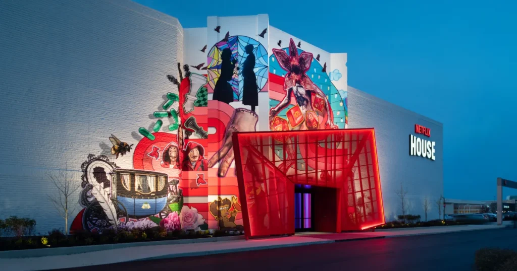Netflix House Philadelphia at dusk, angled view of the red entrance portal flanked by a mural featuring Stranger Things, Bridgerton, and Squid Game characters.