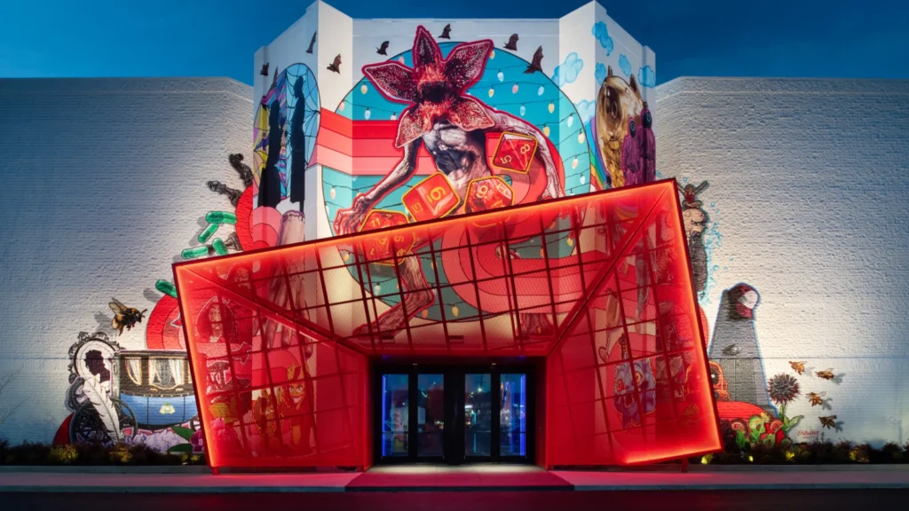 Netflix House Philadelphia exterior at dusk — angular red entrance portal against a large-scale mural featuring Stranger Things, Squid Game, and Wednesday characters. Sparks-designed retail experience.