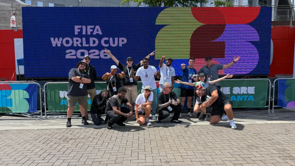 Sparks fan experience team at Mercedes-Benz Stadium during FIFA World Cup 2026 — group photo in front of the tournament LED wall at the "We Are Atlanta" fan zone.