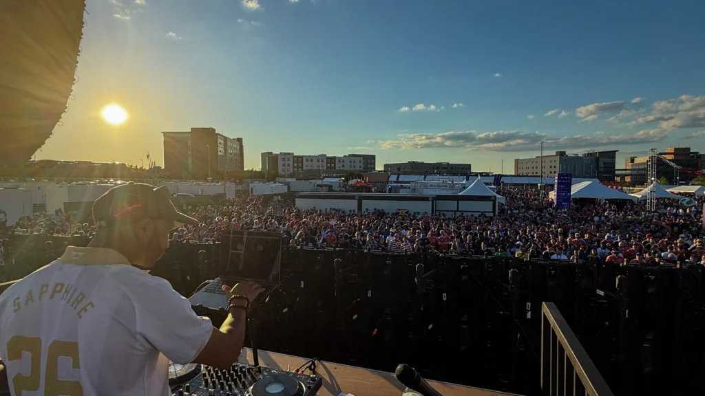 DJ set at golden hour during the Sparks-produced FIFA World Cup 2026 fan experience in Boston — thousands of fans in the fan zone at sunset, with a live music stage overlooking the crowd.