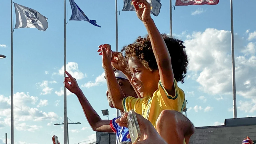 Fan celebration moment at the Sparks-produced FIFA World Cup 2026 fan experience in Philadelphia — young fan in a Brazil jersey cheering under a sky of ceremonial flags.
