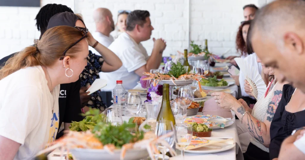 Guests seated at the shared Fruits de Mer lunch hosted by Sparks at Angela's in Margate during the UK Creative Festival 2026, with Rebecca Strickson-illustrated hand fans on the table.