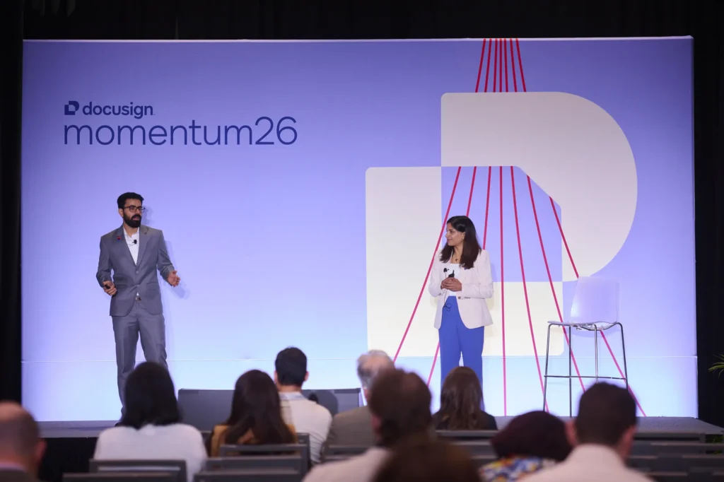 Two presenters delivering a live product demonstration on the main stage at Docusign Momentum 2026.