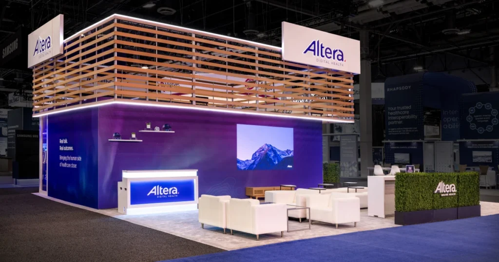 Altera Digital Health booth at HIMSS 2026 featuring a wood-slat pergola, purple LED-lit walls with 'Real talk. Real outcomes.' messaging, a mountain video wall, white lounge seating, and a manicured green hedge — Sparks-designed environment at the Venetian Convention & Expo Center in Las Vegas.
