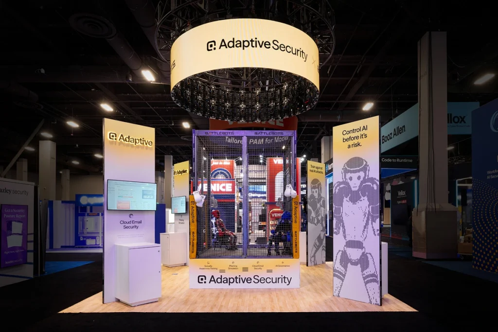Sparks-designed and built Adaptive Security 20x20 exhibit at Black Hat 2026 with a circular halo ceiling structure, caged BattleBots-themed deepfake defense demo, and "Control AI before it's a risk" branded walls at Mandalay Bay Convention Center in Las Vegas.