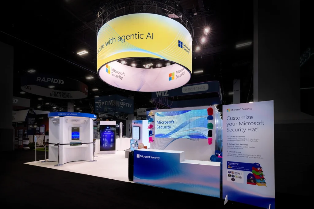 Sparks-designed and built Microsoft Security 30x30 exhibit at Black Hat 2026 with a circular LED halo displaying "Secure with agentic AI," an Agentic AI Arena demo, and a custom Microsoft Security hat-station giveaway at Mandalay Bay Convention Center in Las Vegas.