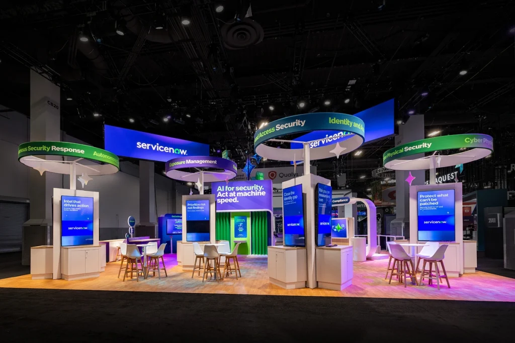 Sparks-designed and built ServiceNow 50x40 flagship exhibit at Black Hat 2026 with five suspended signage rings labeling security tracks — Exposure Management, Identity and Access, Cyber Physical Security, Autonomous Response — around a central "AI for security. Act at machine speed." video wall at Mandalay Bay Convention Center in Las Vegas.