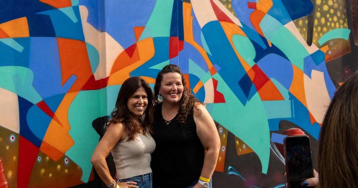 Two Sparks-hosted CEMA Summit 2026 attendees pose for a portrait in front of a bold orange-and-blue abstract mural during the Sparks-led walking tour of Toronto's Graffiti Alley.
