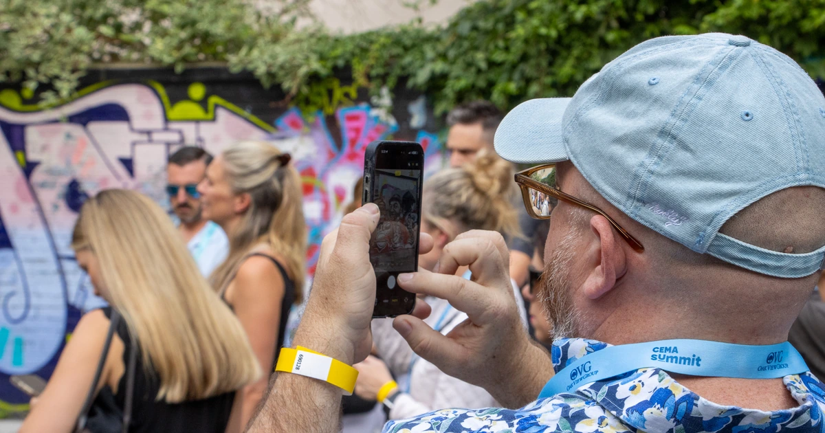 A Sparks-hosted CEMA Summit 2026 attendee — CEMA Summit lanyard visible — photographing a graffiti mural with his phone during the Sparks-led walking tour of Toronto's Graffiti Alley.