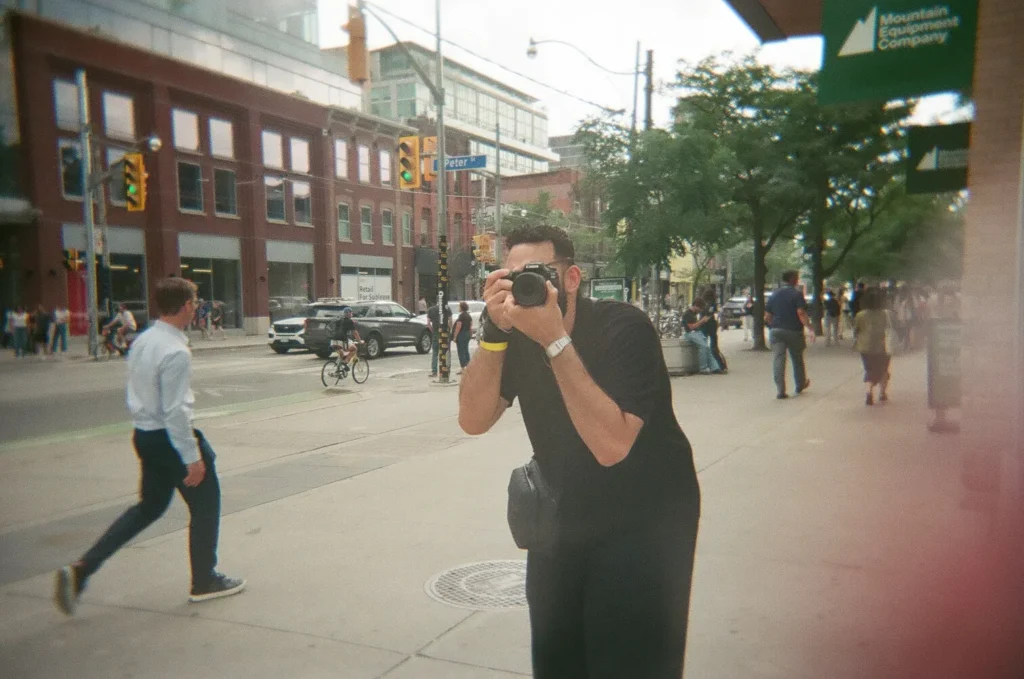 Sparks-hosted CEMA Summit 2026 disposable-camera photo — a CEMA Summit attendee holds up a disposable camera to photograph a Toronto street corner during the Sparks-led Graffiti Alley walking tour.