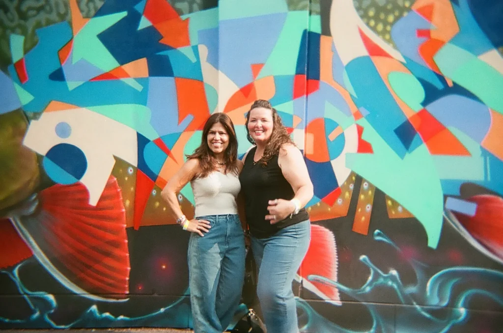 Sparks-hosted CEMA Summit 2026 disposable-camera photo — two CEMA Summit attendees pose in front of a bold colorful geometric abstract mural in Toronto's Graffiti Alley during the Sparks-led walking tour.