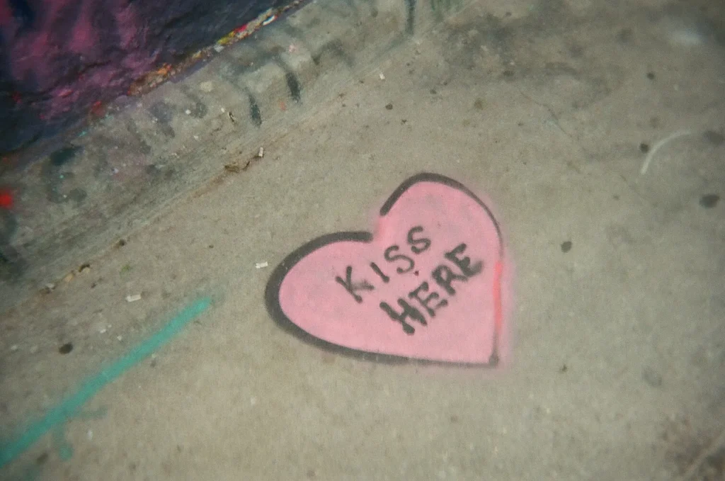 Sparks-hosted CEMA Summit 2026 disposable-camera photo — a stenciled pink heart with the words 'Kiss Here' painted on a Toronto sidewalk, captured during the Sparks-led Graffiti Alley walking tour.