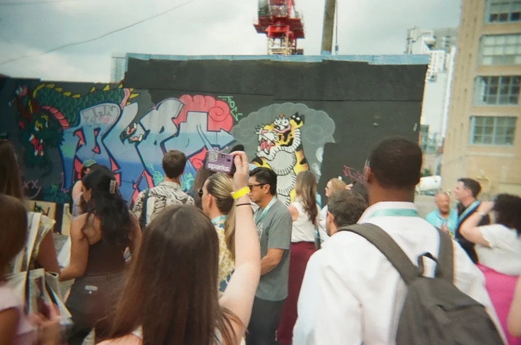 Sparks-hosted CEMA Summit 2026 disposable-camera photo — a group of CEMA Summit attendees photographs a tiger mural in Toronto's Graffiti Alley during the Sparks-led walking tour.