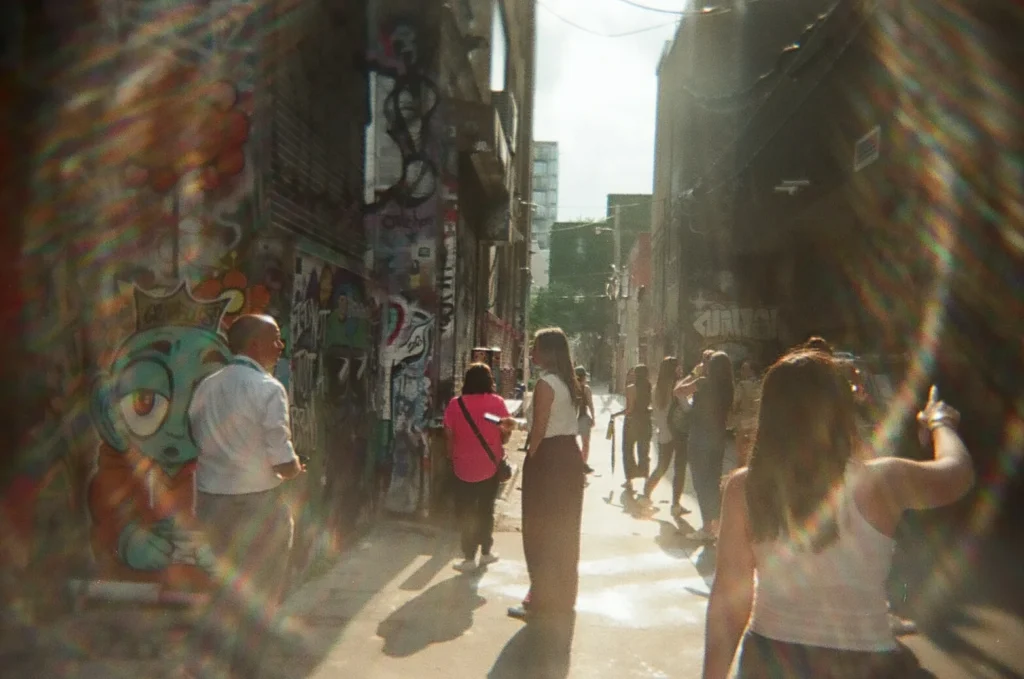 Sparks-hosted CEMA Summit 2026 disposable-camera photo — sunlight streams through Toronto's Graffiti Alley as CEMA Summit attendees make their way through on the Sparks-led walking tour.