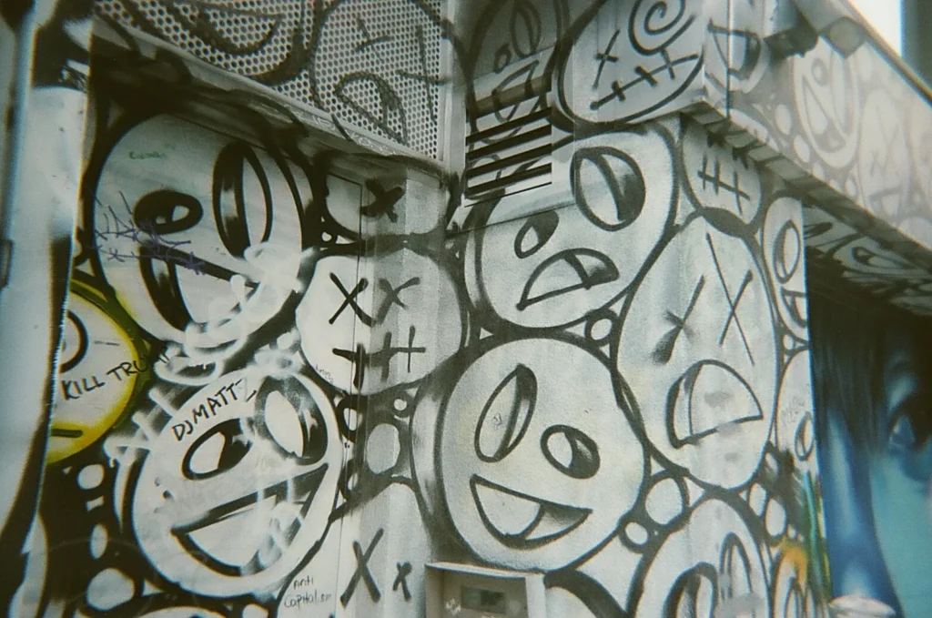 Sparks-hosted CEMA Summit 2026 disposable-camera photo — a KAWS-inspired mural of stacked cartoon faces with X eyes in Toronto's Graffiti Alley, captured on the Sparks-led CEMA Summit walking tour.