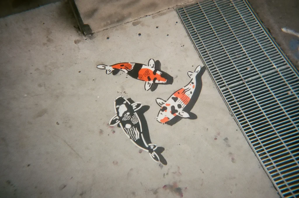 Sparks-hosted CEMA Summit 2026 disposable-camera photo — a school of koi fish street decal on a downtown Toronto sidewalk next to a drain grate, captured during the Sparks-led CEMA Summit Graffiti Alley walking tour.