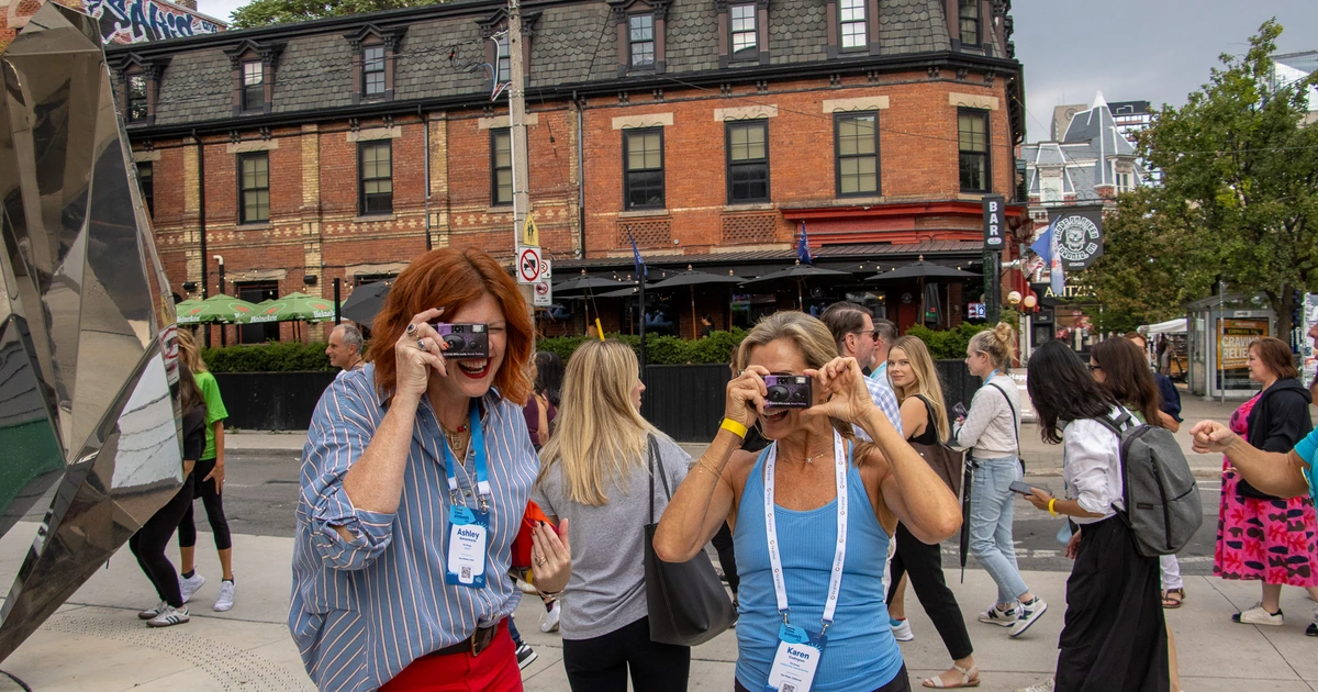Sparks-hosted CEMA Summit 2026 attendees Ashley and Karen using disposable cameras on a Toronto street corner during the Sparks-led walking tour of Graffiti Alley.