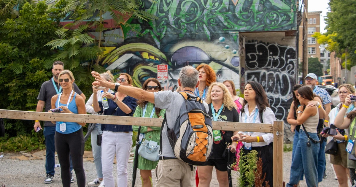 A guide leading Sparks-hosted CEMA Summit 2026 attendees through Toronto's Graffiti Alley, pointing out details in a large green mural during the Sparks-led walking tour.