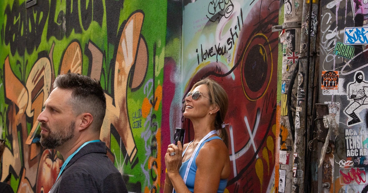 Sparks-hosted CEMA Summit 2026 attendees stand beside an "I love you, still" mural and a sticker-covered post in Toronto's Graffiti Alley during the Sparks-led walking tour.