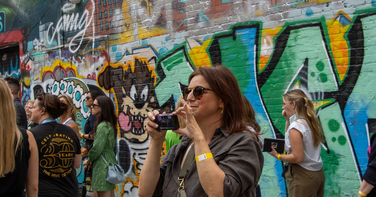 A Sparks-hosted CEMA Summit 2026 attendee photographs a Tasmanian Devil–style mural with a disposable camera during the Sparks-led walking tour of Toronto's Graffiti Alley.