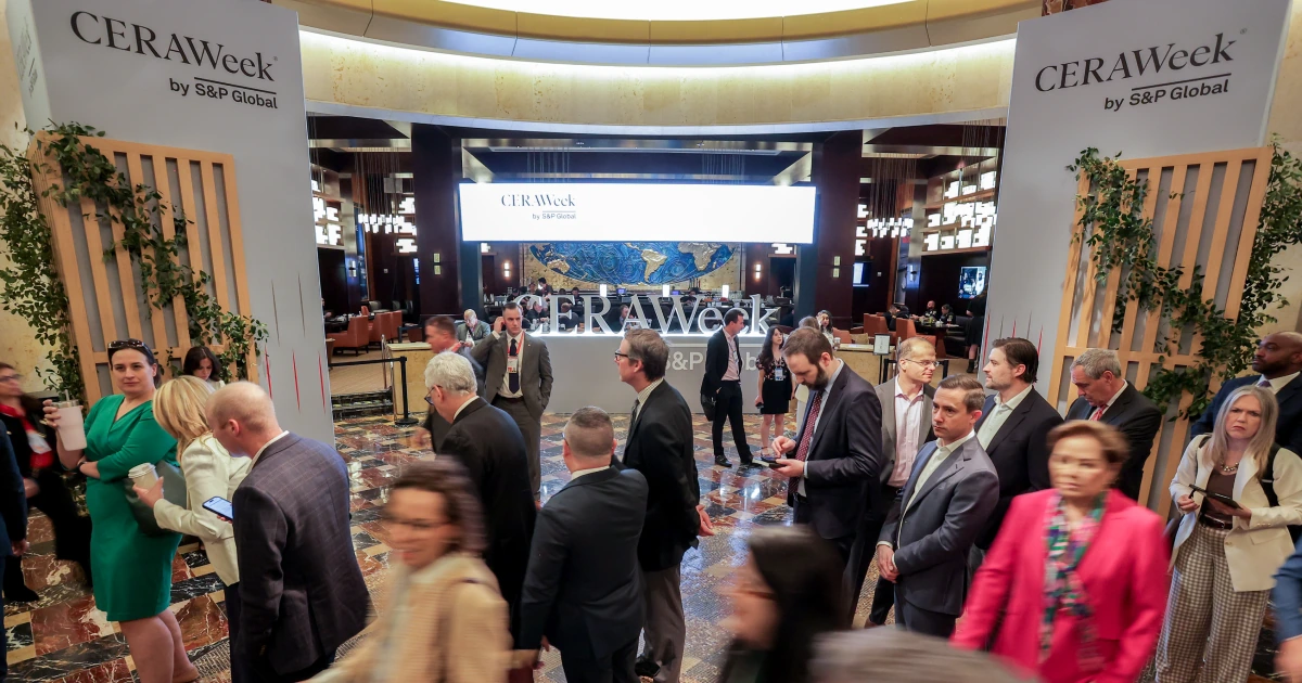 The Sparks-designed CERAWeek by S&P Global branded entrance gateway with lush green florals in the Hilton Americas-Houston lobby at CERAWeek 2026 — arriving delegates flow through the archway toward registration on the opening day of the 44th annual energy conference by S&P Global.