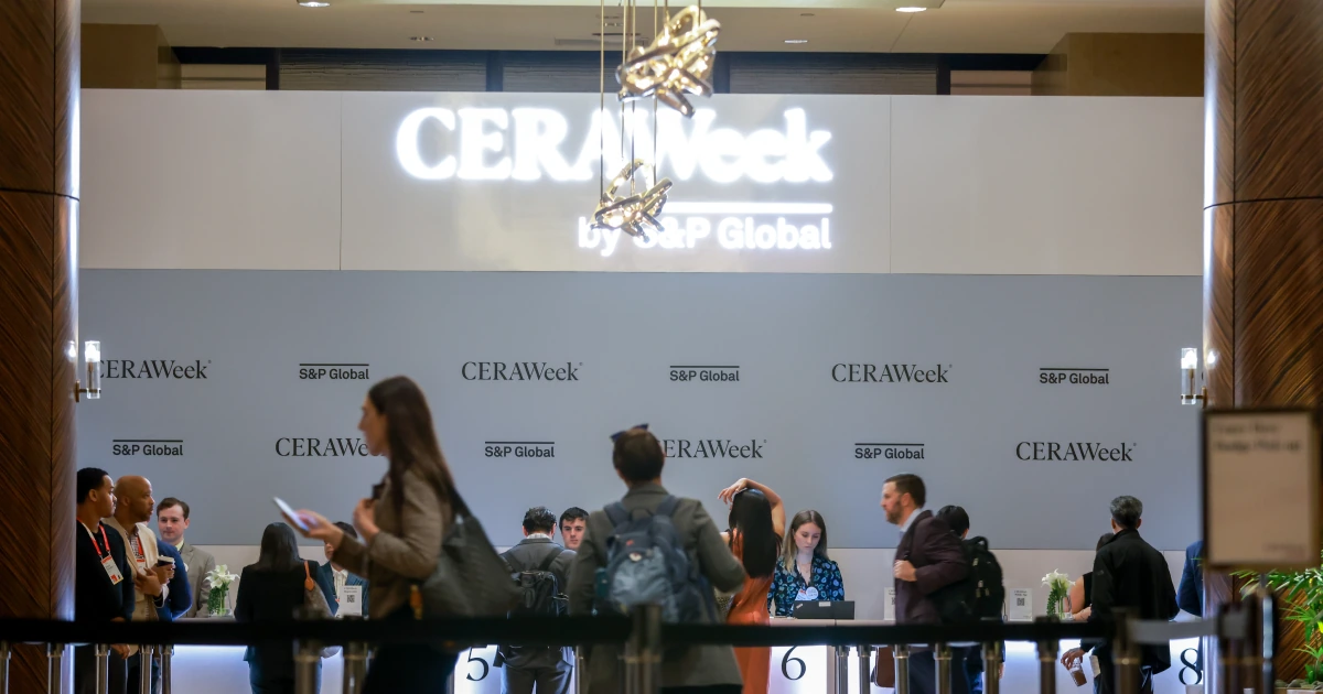 Delegates check in at the Sparks-produced CERAWeek 2026 by S&P Global registration counter at the Hilton Americas-Houston — numbered check-in stations under the illuminated CERAWeek by S&P Global signage and full-wall step-and-repeat on the opening morning of the five-day energy conference.
