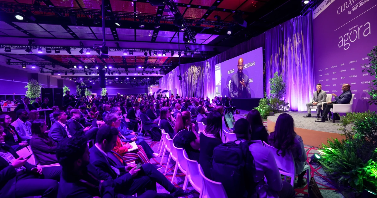 A fireside-chat session on the Sparks-produced Nasdaq Amphitheater stage in the Innovation Agora at CERAWeek 2026 by S&P Global — magenta willow-inspired scenic and CERAWeek by S&P Global backdrop with a packed audience at the George R. Brown Convention Center in Houston.