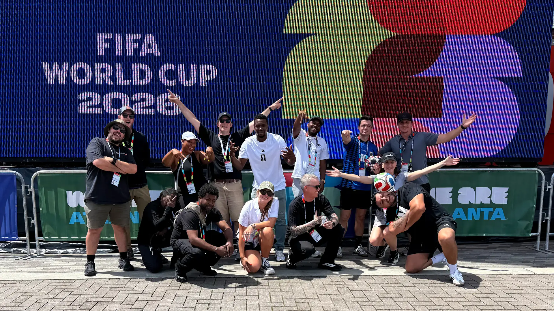 The Sparks production team on-site at the FIFA World Cup 2026 Atlanta host city — Sparks producers, designers, and brand ambassadors pose for a group photo in front of the FIFA World Cup 2026 LED backdrop and 'WE ARE ATLANTA' branded barricades at the Sparks-produced Stadium Fan Experience Town Square outside Mercedes-Benz Stadium in Atlanta.