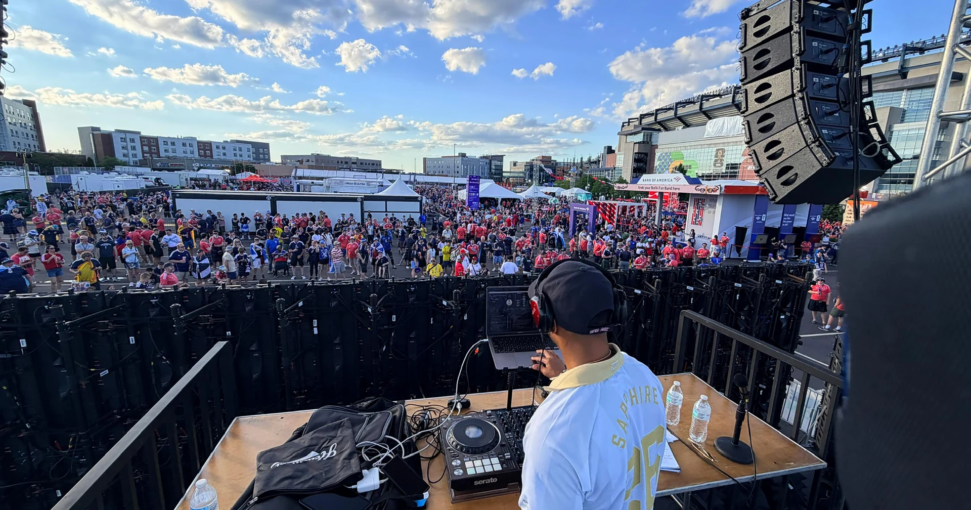A DJ performs on the Sparks-produced Town Square main stage at golden hour in front of a massive fan crowd at the FIFA World Cup 2026 Boston host city — the Sparks-designed centerpiece of the Stadium Fan Experience outside Gillette Stadium in Foxborough, Massachusetts.