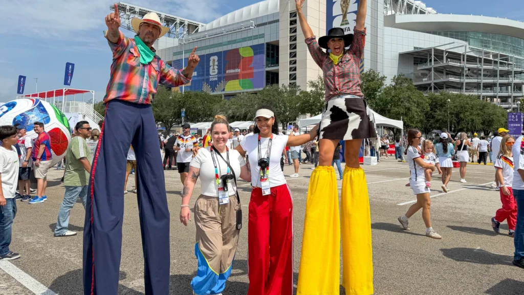 Two Texas-themed stilt walkers pose with Sparks brand ambassadors at the Sparks-produced Stadium Fan Experience Town Square outside NRG Stadium at the FIFA World Cup 2026 Houston host city — an example of the locally cast programming Sparks brought to each of the seven US host cities.