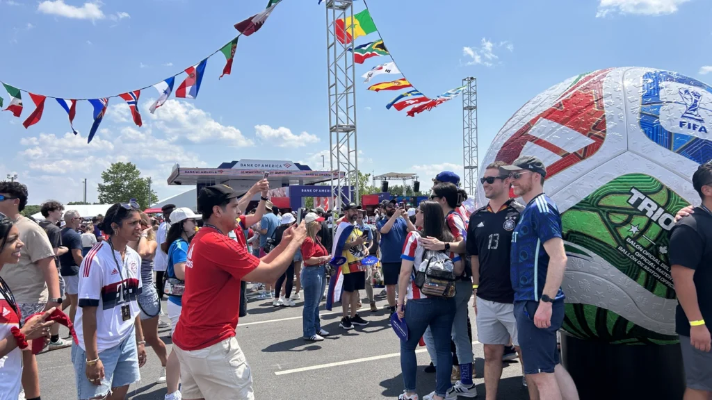 Fans photograph themselves at the Sparks-produced giant Trionda match-ball sculpture under a canopy of national flags at the FIFA World Cup 2026 Stadium Fan Experience Town Square — a Sparks-designed iconic FIFA touchpoint recreated at every one of the seven US host cities.