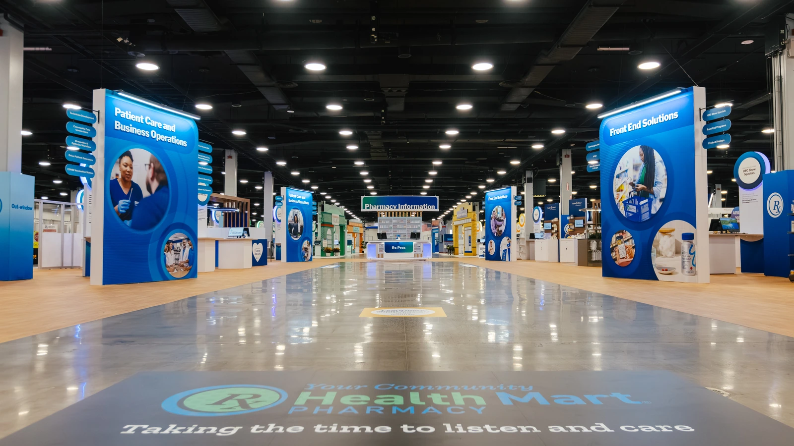The Sparks-designed central aisle of the Main Street USA-themed McKesson ideaShare 2025 tradeshow floor — anchored by the HealthMart 'Taking the time to listen and care' floor mural at the Gaylord Opryland Resort & Convention Center in Nashville.