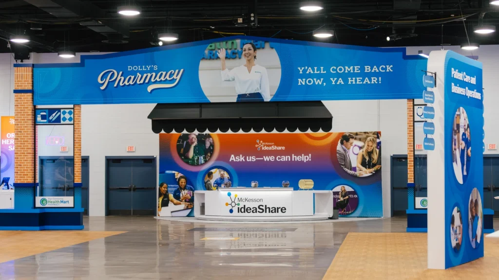 The Sparks-designed Dolly's Pharmacy exit facade with 'Y'all Come Back Now, Ya Hear!' hand-lettered signage on the Main Street USA-themed McKesson ideaShare 2025 tradeshow floor at the Gaylord Opryland Resort & Convention Center in Nashville.
