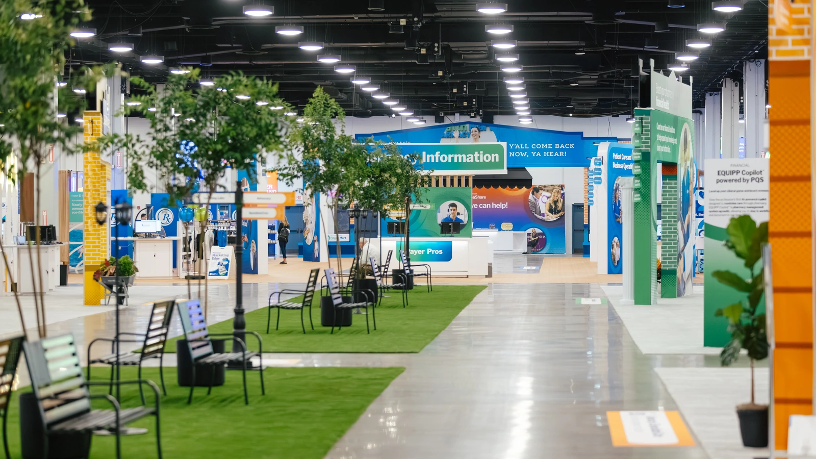 Wide view of the Sparks-designed Main Street USA-themed McKesson ideaShare 2025 tradeshow floor — pharmacy, information, and solution storefronts line the central aisle at the Gaylord Opryland Resort & Convention Center in Nashville.