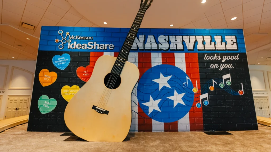The Sparks-designed 'Nashville Looks Good on You' photo moment at McKesson ideaShare 2025 — an oversized acoustic guitar leans against a heart-and-star mural at the Main Street USA-themed tradeshow entrance at the Gaylord Opryland Resort & Convention Center in Nashville.
