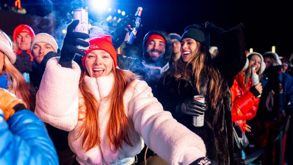 Fan celebration at Sparks-produced Michelob ULTRA Summit, Canyons Village at Park City — guests in Michelob ULTRA beanies raise cans in a Team USA cheer moment during the Milano Cortina 2026 Winter Olympics closing weekend.
