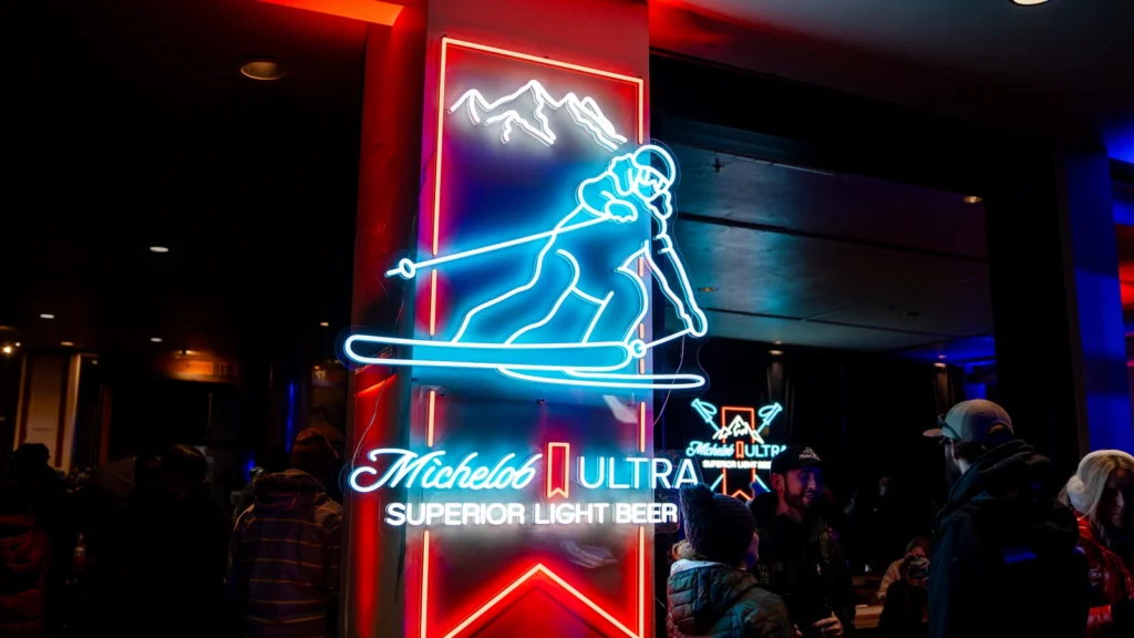 Michelob ULTRA neon skier signage at Sparks-designed ULTRA Summit, Canyons Village at Park City — illuminated "Superior Light Beer" feature at the invite-only takeover during the closing weekend of the Milano Cortina 2026 Winter Olympics.