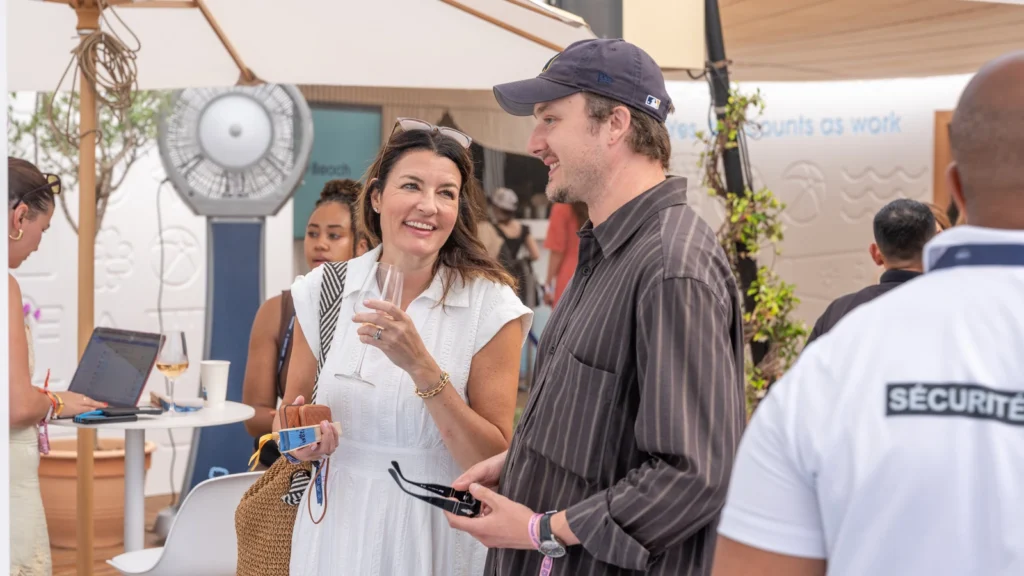 Two attendees networking over wine in front of the "Yes, this counts as work" embossed wall inside the Sparks-designed Salesforce Beach lounge at Cannes Lions 2026.