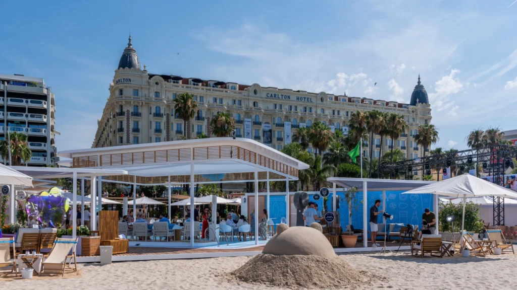 Wide daytime view of the Sparks-designed Salesforce Beach activation with the InterContinental Carlton Cannes hotel and palm trees rising behind La Croisette at Cannes Lions 2026.
