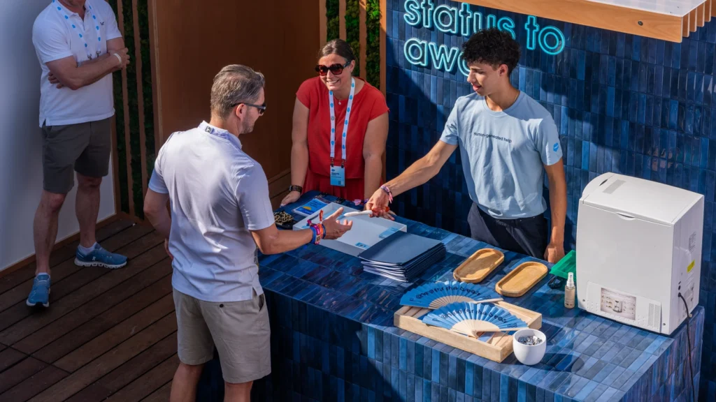 Salesforce Beach team member handing an "@here for the breeze" fan to a guest at the "Set your status to away" activation at the Sparks-designed Cannes Lions 2026 experience.