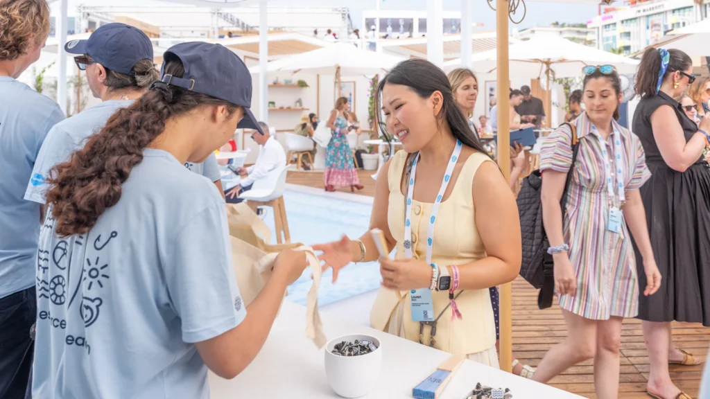 Salesforce Beach team member Lauren handing a Cannes tote bag with branded merchandise to a guest at the Souvenir Stop inside the Sparks-designed Cannes Lions 2026 activation.