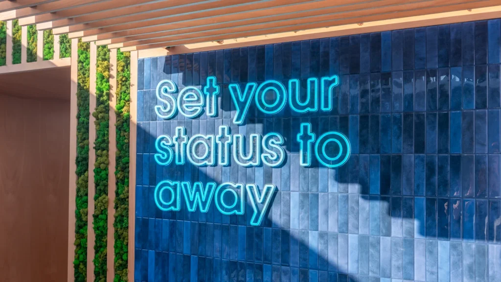 Cyan "Set your status to away" neon signage on a blue-tiled wall with wood-slat pergola and moss vertical accents at the Sparks-designed Salesforce Beach at Cannes Lions 2026.